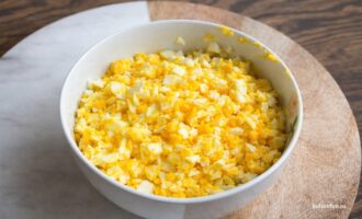 Измельченные вареные яйца в миске на деревяннои доске