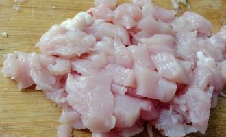 Нарезанное кубиками сырое филе куриной грудки на разделочной доске