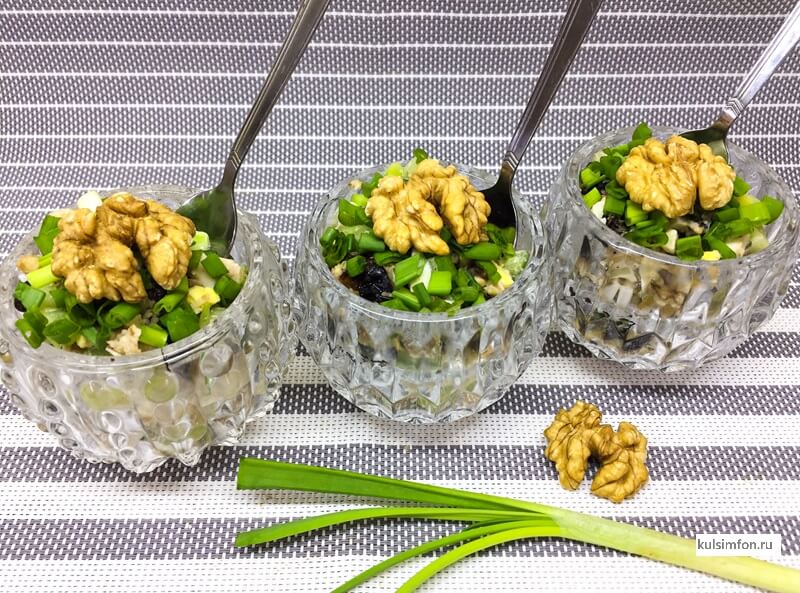 Салат с курицей, черносливом, грецким орехом и свежим огурцом, поданный порционно в креманках и украшенный зеленым луком и половинками орехов.