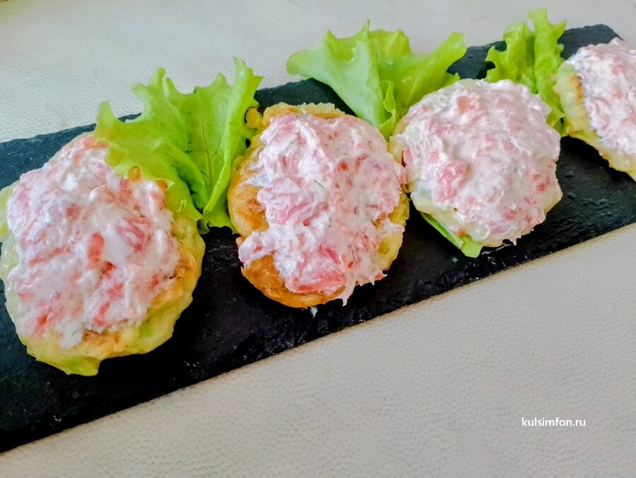 Кабачковые оладьи с творожным сыром и слабосоленой кетой, украшенные зеленью на тарелке