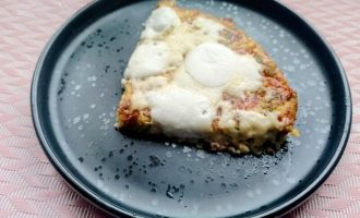 Кусочек картофельной лепешки с колбасой и сыром на тарелке перед подачей.