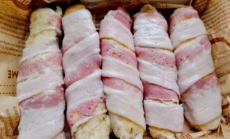 Куриные колбаски, обмотанные ломтиками бекона перед запеканием