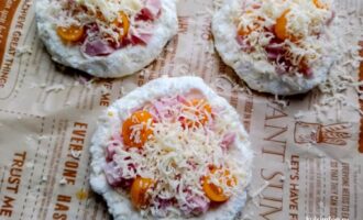 Мини-пиццы, посыпанные тертым сыром перед отправкой в духовку