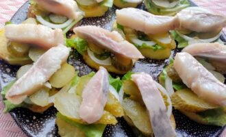 Подача закуски с картофелем, сельдью и зеленью на блюде