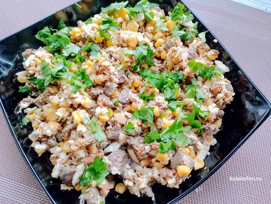 Салат с куриной печенью и кукурузой с зеленью на тарелке
