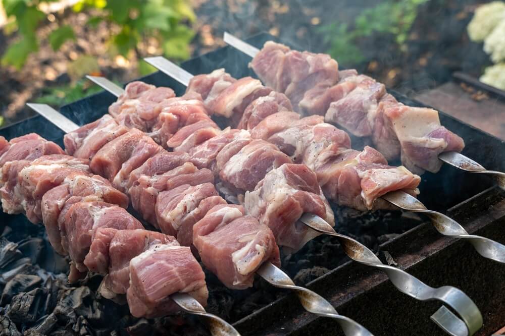 Сырое мясо для шашлыка на шампурах над углями